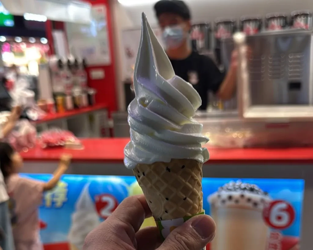Mixue marketing strategy in action: a S$0.40 soft serve ice cream cone held up at a Shenzhen store with red brand signage in the background