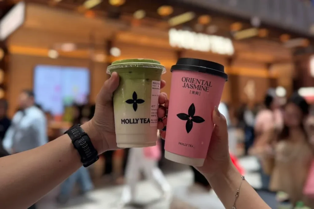 Two people holding Molly Tea cups with the four-petal logo in a busy store